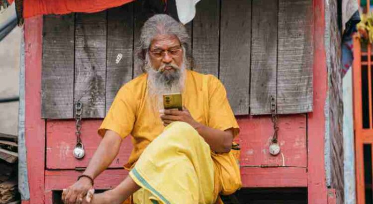 An elderly man in traditional attire uses a smartphone, sitting outdoors in Varanasi., tags: indiens mobile - pexel